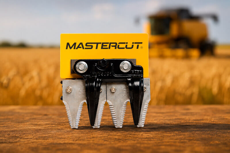 Sistema de corte mastercut, com lamina dupla e dedo triplo. Produto exposto sobre mesa, ao fundo, uma colheitadeira trabalha no campo.