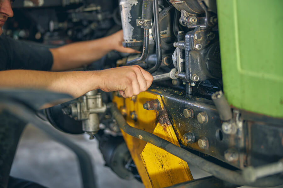Profissional realizando manutenção em máquina agrícola, com chave específica.